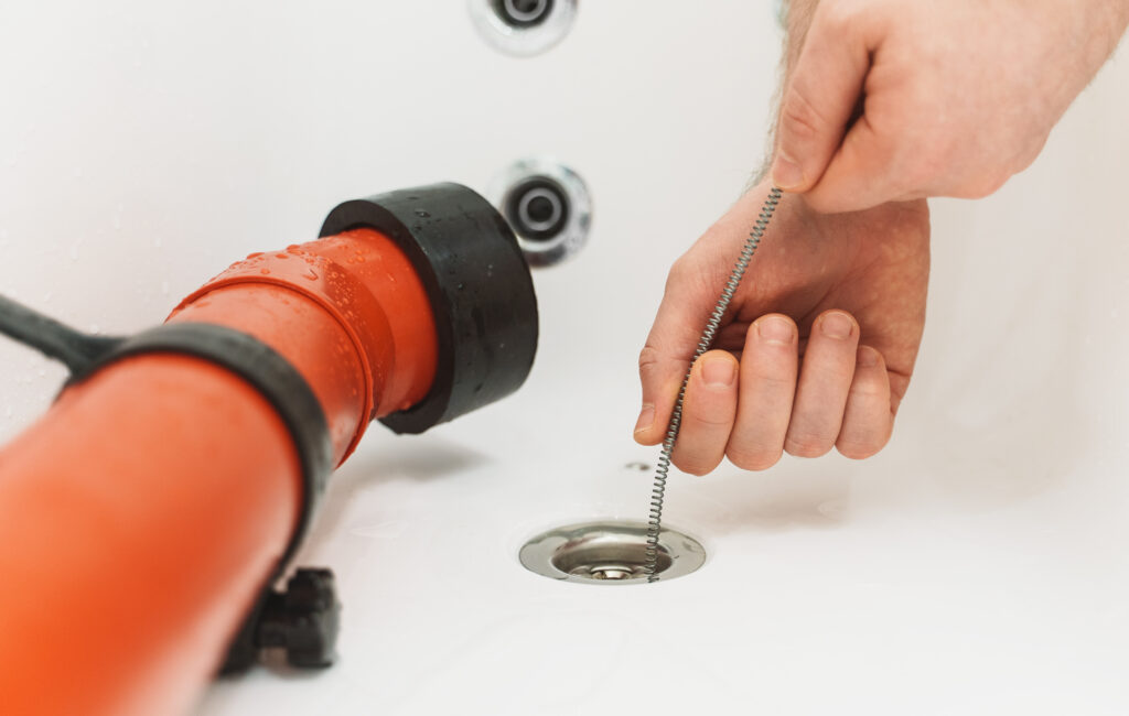 Plumber using drain snake to unclog bathtub.